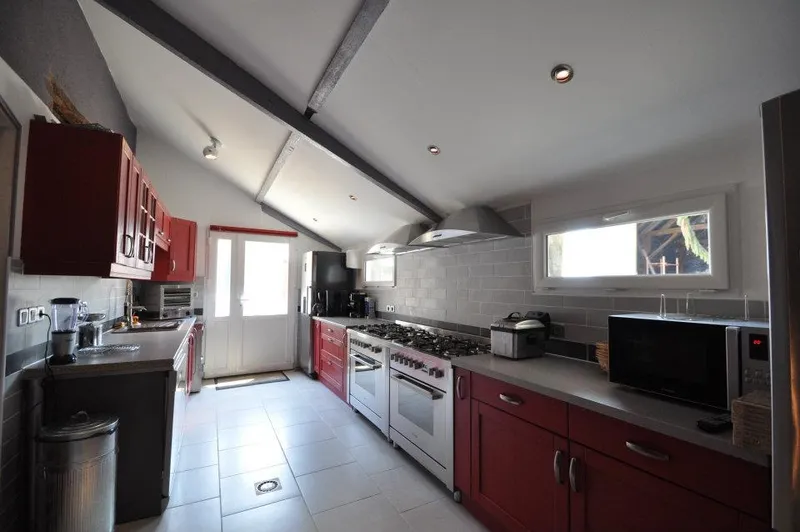 Cuisine équipée avec piano de cuisson six feux, hotte inox et long plan de travail sombre
