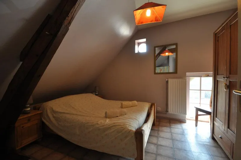 Chambre mansardée avec poutres apparentes, lit double, armoire en bois et fenêtre lumineuse