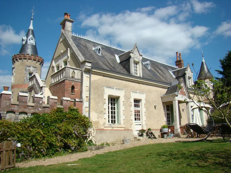 Façade du manoir avec tourelles en pierre et brique, toits d'ardoise et jardin fleuri en premier plan