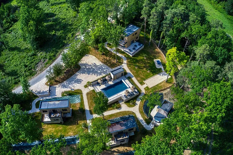 Vue aérienne du domaine avec plusieurs cabanes en bois dispersées dans la forêt de chênes autour de la piscine