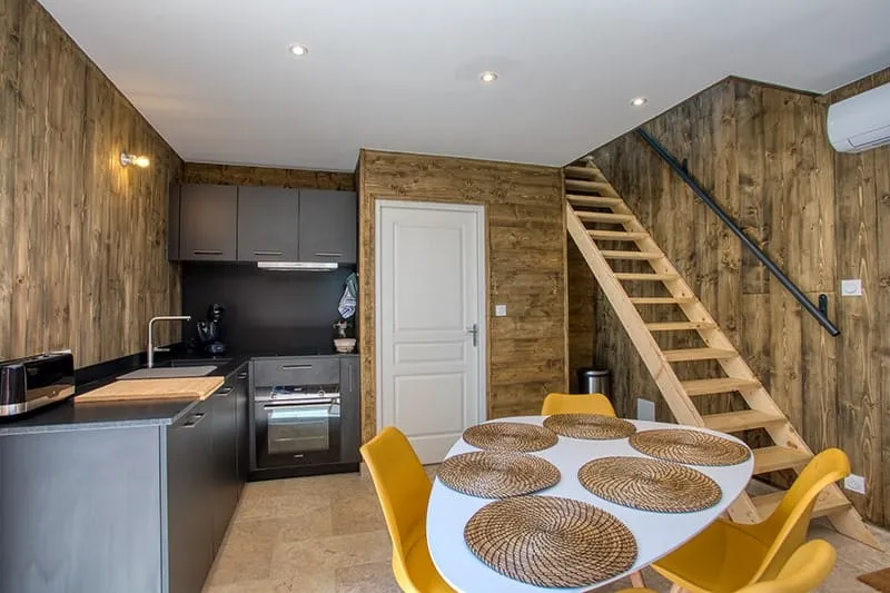 Cuisine équipée d'une cabane avec plan de travail noir, four intégré et table entourée de chaises jaunes