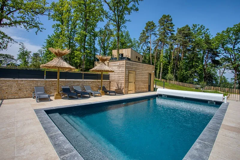 Piscine chauffée entourée de transats, parasols en paille tressée et terrasse en pierre claire