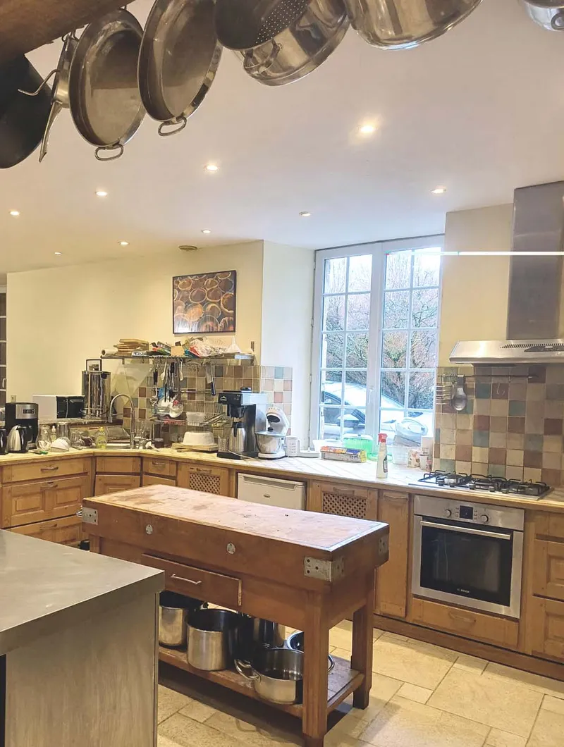 Cuisine équipée avec îlot central en bois, casseroles suspendues et four professionnel