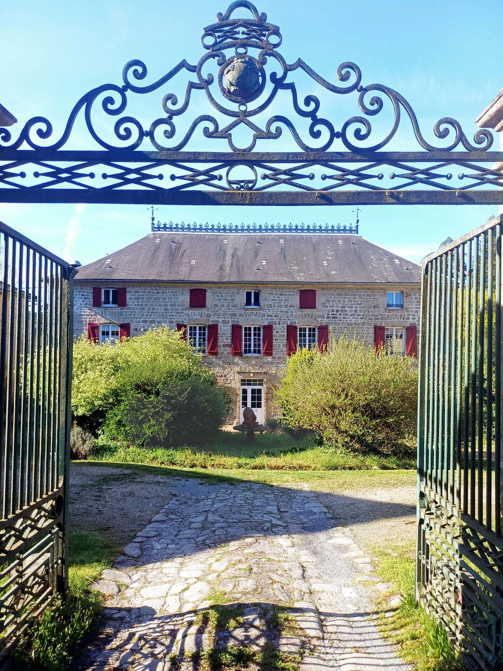 Gîte de groupe Manoir de Plainartige à Nedde — Portail en fer forgé ouvrant sur la façade en pierre blonde du manoir et son parc arboré, capacité 45 personnes