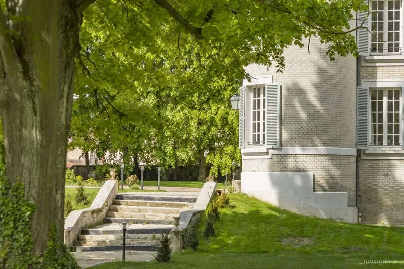 Angle du château vu du parc, escalier en pierre menant à la pelouse, grand arbre au feuillage vert au premier plan