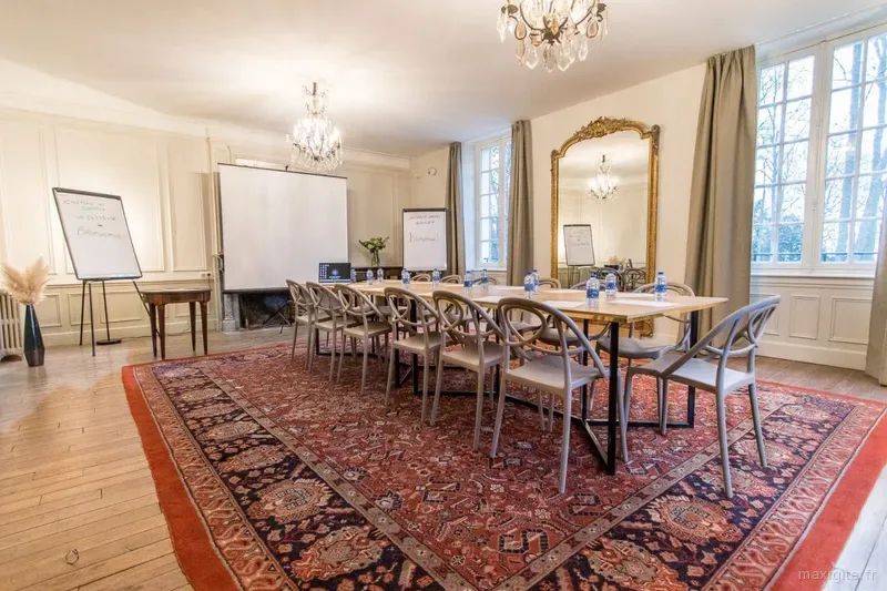 Grande salle de réception avec longue table de réunion, chaises grises, lustres en cristal et grand miroir doré