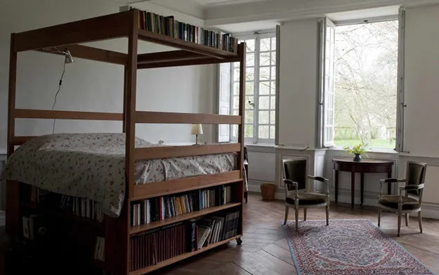 Chambre lumineuse avec lit à baldaquin en bois flanqué de bibliothèques garnies et hautes fenêtres sur le parc