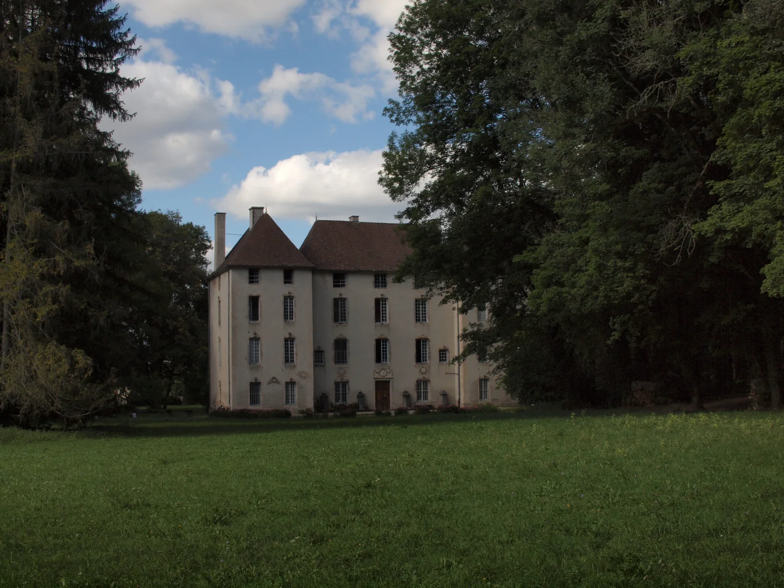 Gîte de groupe Château de Lusigny à Lusigny-sur-Ouche — Façade sud du château vue depuis la prairie, toitures d'ardoise et tourelle entourées de grands arbres, capacité 19 personnes
