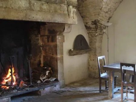 Salle de vie voûtée avec grande cheminée de pierre allumée et four à pain ancien encastré dans le mur