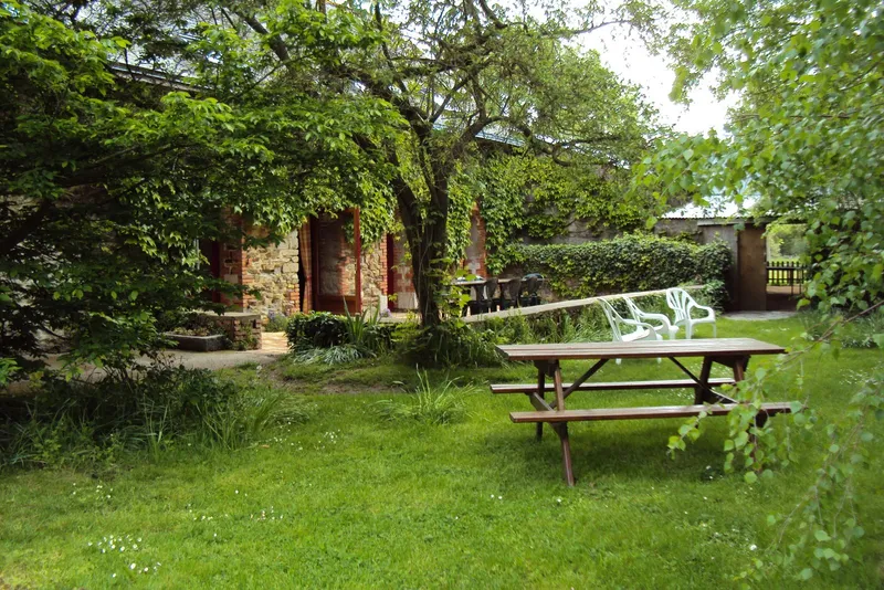 Jardin arboré avec table de pique-nique en bois et façade du gîte visible en arrière-plan