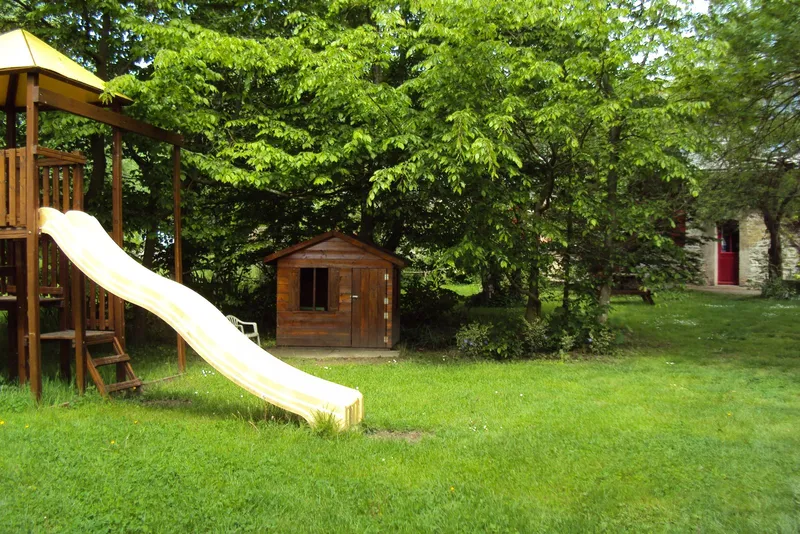 Aire de jeux extérieure avec toboggan en bois et cabane, entourée de grands arbres dans le parc