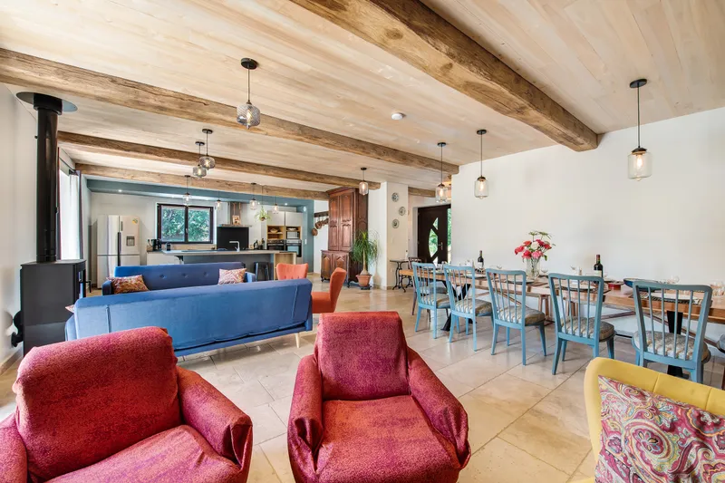 Grand séjour aux poutres apparentes avec canapé bleu, fauteuils colorés et longue table conviviale