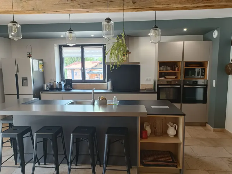 Cuisine équipée avec îlot central noir, tabourets hauts et fenêtre donnant sur la campagne