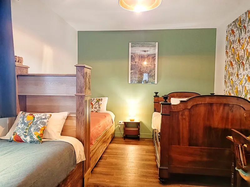 Chambre avec trois lits en bois, tête de lit ancienne et papier peint à motifs de perroquets