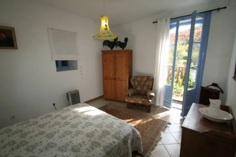 Chambre lumineuse avec lit fleuri, armoire en bois et porte-fenêtre bleue ouvrant sur la terrasse
