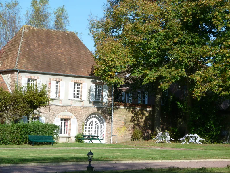 Vue du domaine avec bâtisse en briques et toit de tuiles, banc vert et mobilier de jardin blanc sur la pelouse