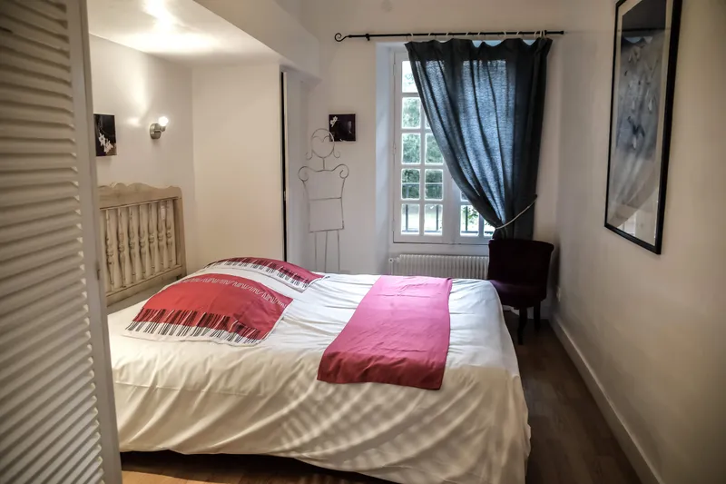 Chambre lumineuse avec grand lit habillé de linge blanc et touches rouges, fenêtre donnant sur le parc