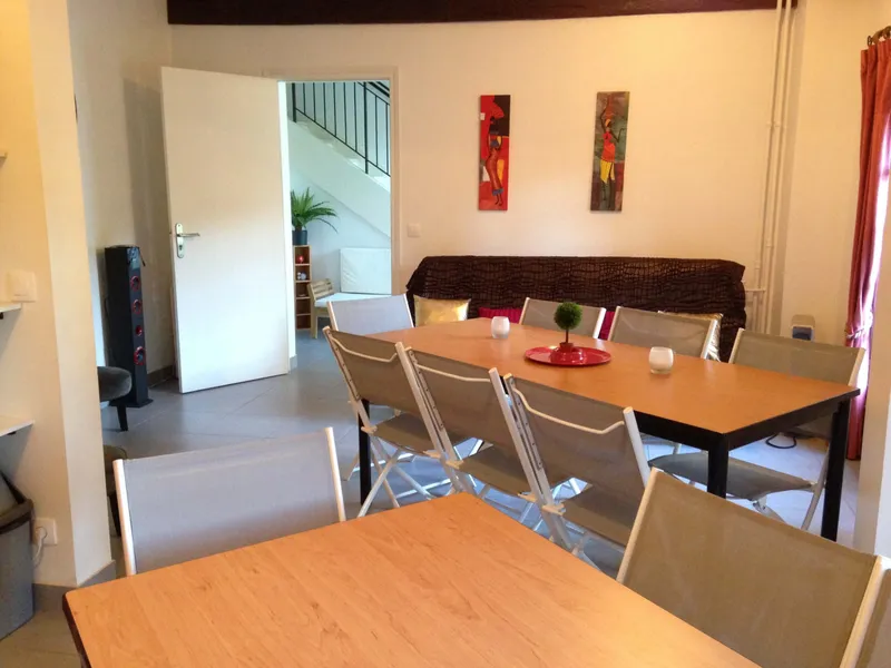 Grand séjour avec longue table en bois pour dix convives, chaises pliantes et canapé en arrière-plan