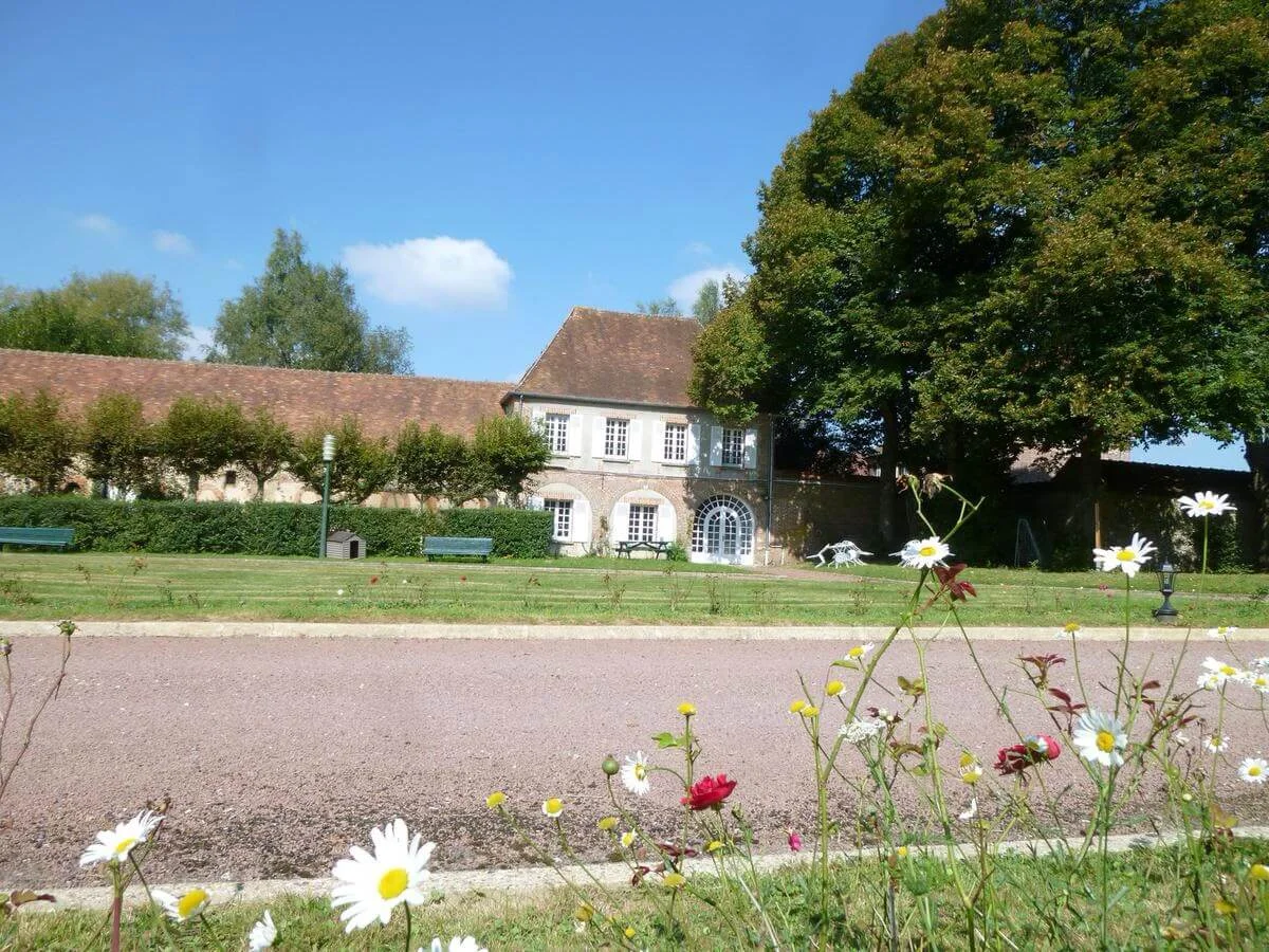 Gîte de groupe Gîte de Groupe du Château de la Houssoye à La Houssoye — Longère en pierre du gîte de groupe bordée d'arbres, avec allée de gravier et marguerites au premier plan, capacité 15 personnes