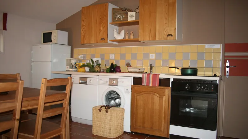 Cuisine équipée avec meubles en bois, crédence carrelée jaune et grise, four, plaques et lave-linge