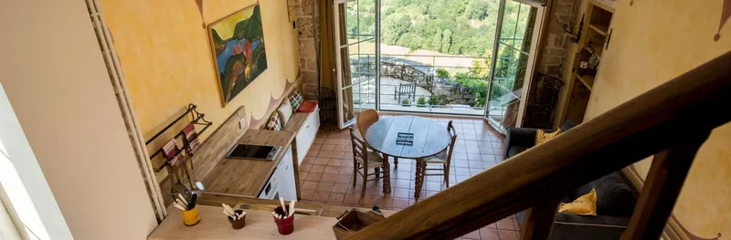 Coin repas en mezzanine avec table ronde en bois, banquette et grande baie vitrée ouvrant sur la vallée boisée
