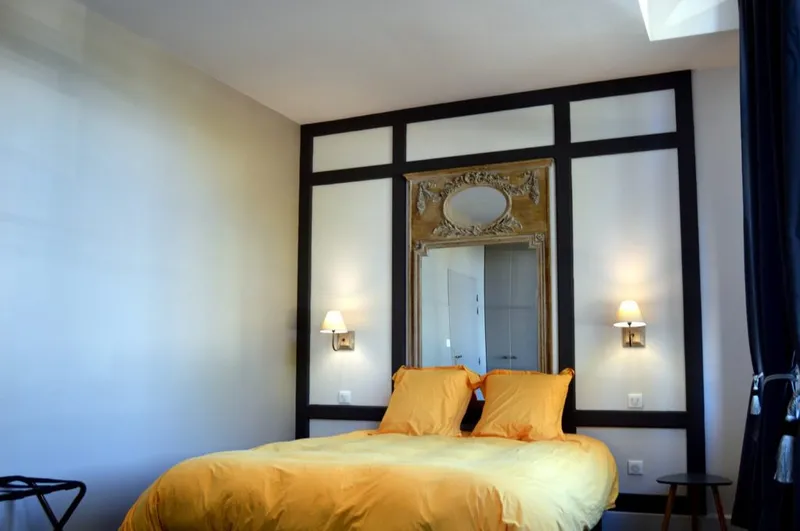 Chambre lumineuse avec grand lit au linge jaune, miroir ancien et appliques murales de part et d'autre du lit