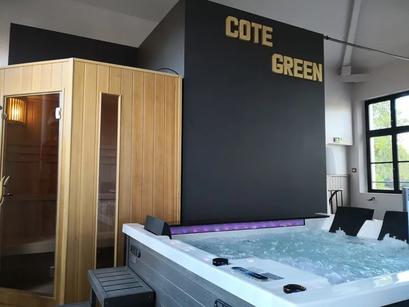 Espace bien-être du gîte avec sauna en bois et spa à bulles, sous l'enseigne lumineuse Côté Green