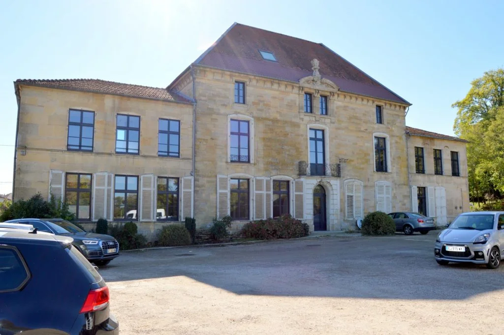Gîte de groupe Côté Green à Combles-en-Barrois — Façade en pierre du château du XVIe siècle abritant le gîte, avec parking gravillonné devant l'entrée, capacité 15 personnes