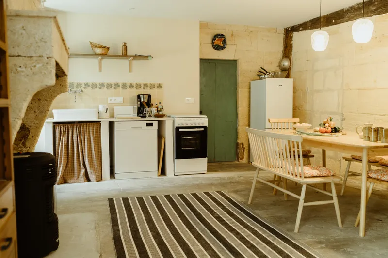 Cuisine en pierre voûtée avec four, lave-vaisselle, réfrigérateur et grande table en bois massif