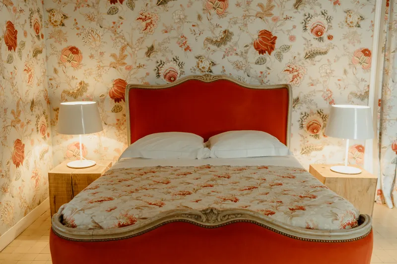 Chambre avec lit double à tête de lit rouge capitonnée et papier peint fleuri rouge et beige