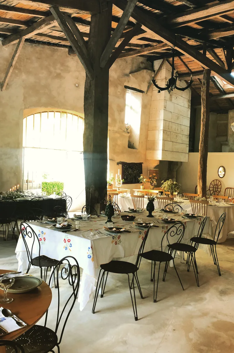 Grande salle de réception en pierre à charpente apparente, tables dressées avec nappes brodées et bougies