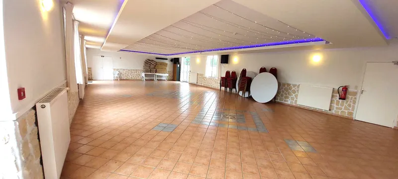 Grande salle de réception au sol carrelé avec plafond tendu étoilé et éclairage bleuté, chaises empilées le long du mur