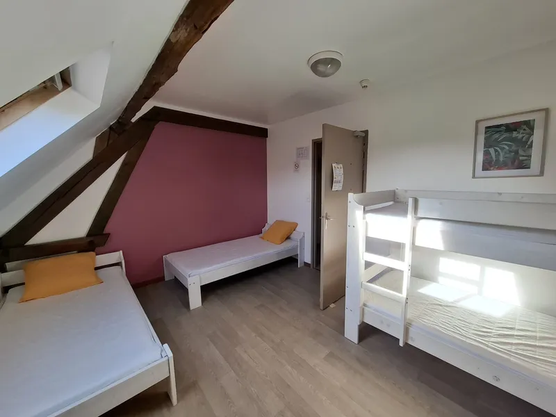 Chambre mansardée avec poutres apparentes, pan de mur rose, lits simples et lit superposé blanc