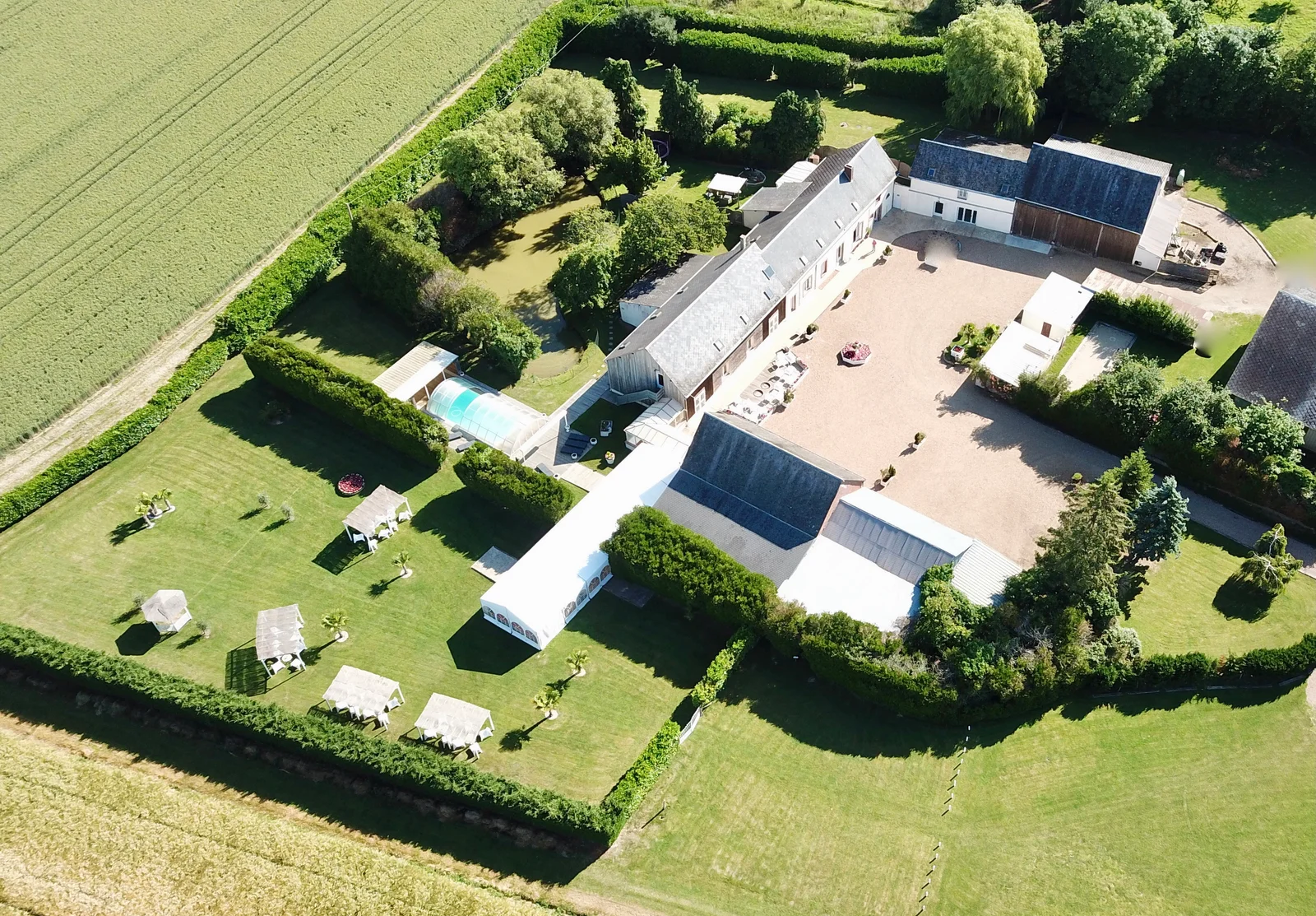 Gîte de groupe Domaine de l'Ozanne à Brou — Vue aérienne du domaine avec bâtisses en pierre et toits d'ardoise, piscine couverte et grand parc arboré clos de haies, capacité 80 personnes