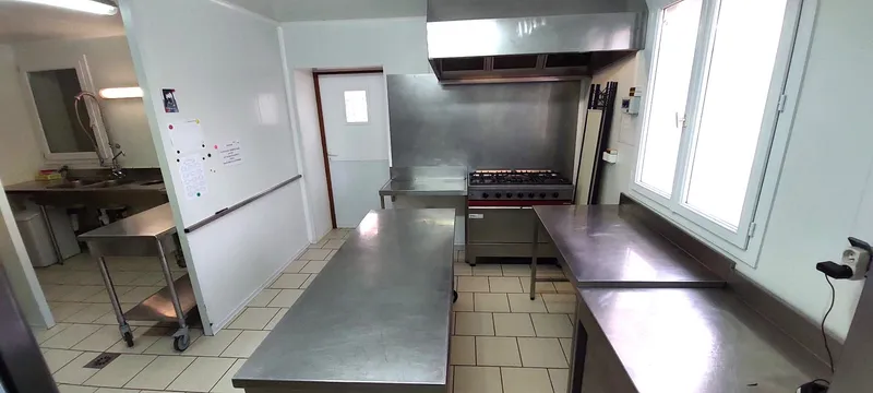 Cuisine professionnelle avec plans de travail en inox, piano de cuisson à plusieurs feux et hotte industrielle