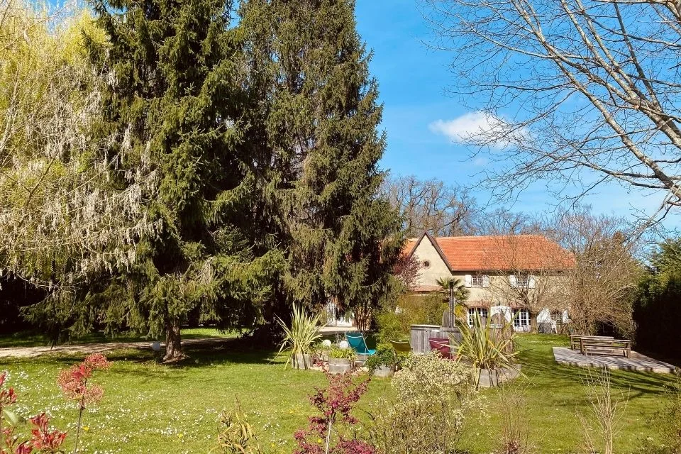 Gîte de groupe Domaine des Deux Clos à Pontiacq-Viellepinte — Bâtisse du domaine entourée de grands sapins et pelouse verdoyante sous un ciel bleu, capacité 31 personnes