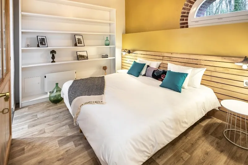Chambre parentale aux murs jaune moutarde avec grand lit en bois et étagères murales blanches