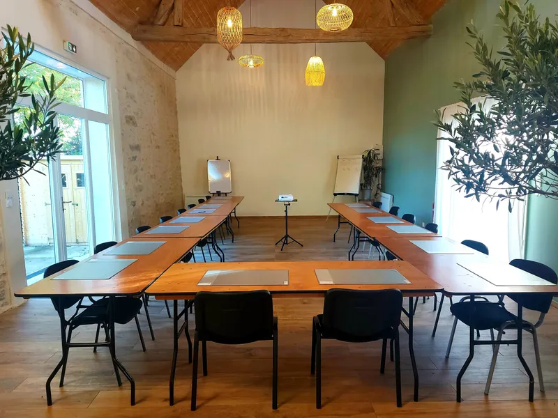 Grande salle voûtée aux poutres apparentes aménagée en U avec tables et chaises pour un séminaire