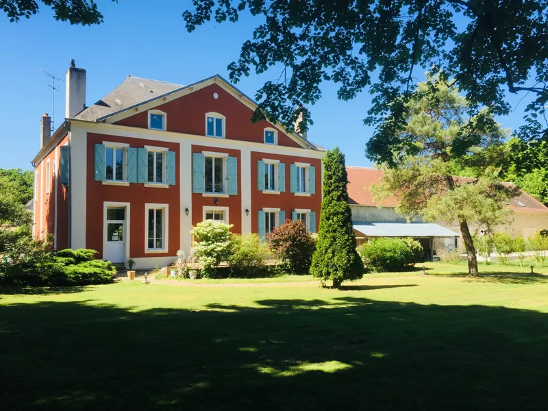 Façade orangée du corps de logis principal aux volets bleu pâle, entourée d'un grand parc arboré