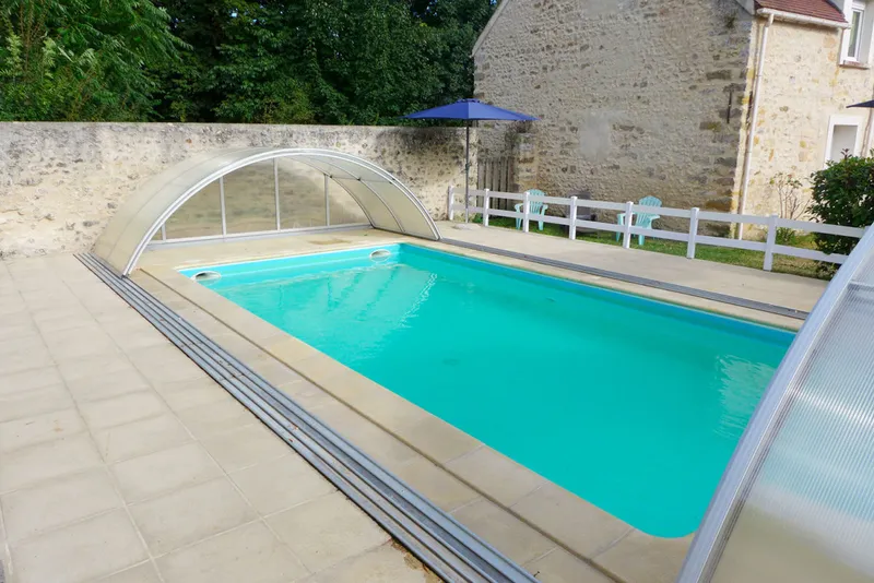 Piscine extérieure avec abri télescopique ouvert, terrasse carrelée, transats et parasol bleu