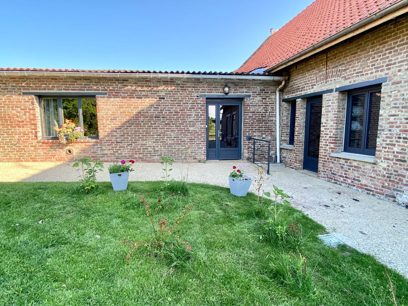 Gîte de groupe Gîte de Groupe Au Cheval Flamand - Ferme Beck à Bailleul — Façade en briques rouges de la ferme rénovée avec portes-fenêtres bleu marine et jardin fleuri, capacité 50 personnes