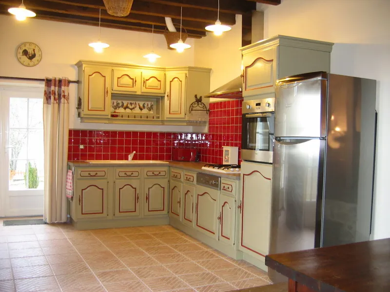 Cuisine équipée avec meubles beiges, crédence en carrelage rouge, four encastré et grand réfrigérateur inox
