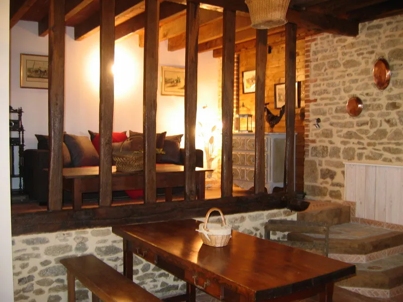 Grande pièce à vivre traditionnelle avec poutres et piliers en bois, canapés, table en bois massif et cheminée en pierre
