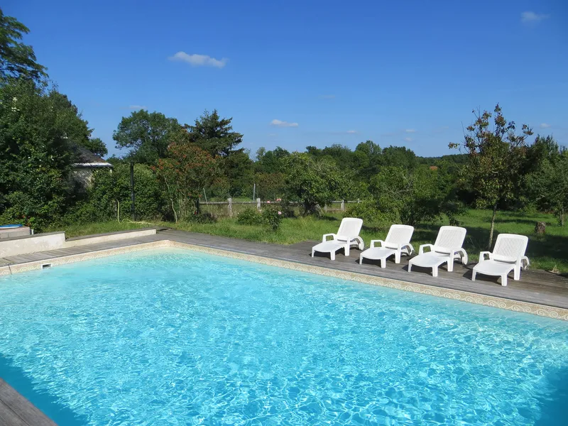 Piscine extérieure avec transats blancs alignés sur une terrasse en bois face à la campagne