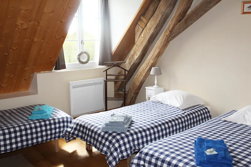 Chambre mansardée avec trois lits simples à parures à carreaux bleus et blancs sous poutres anciennes