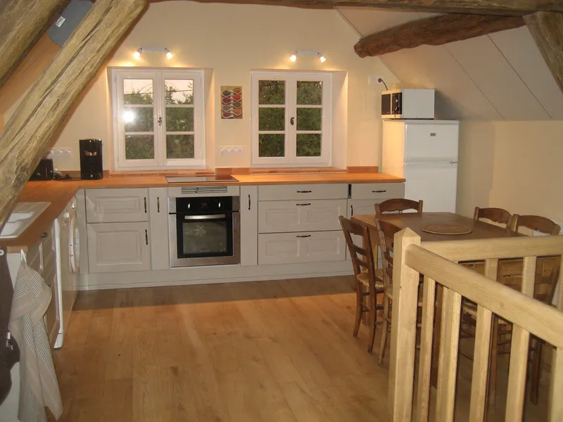 Cuisine sous charpente en bois avec plan de travail, four encastré et grande table à manger