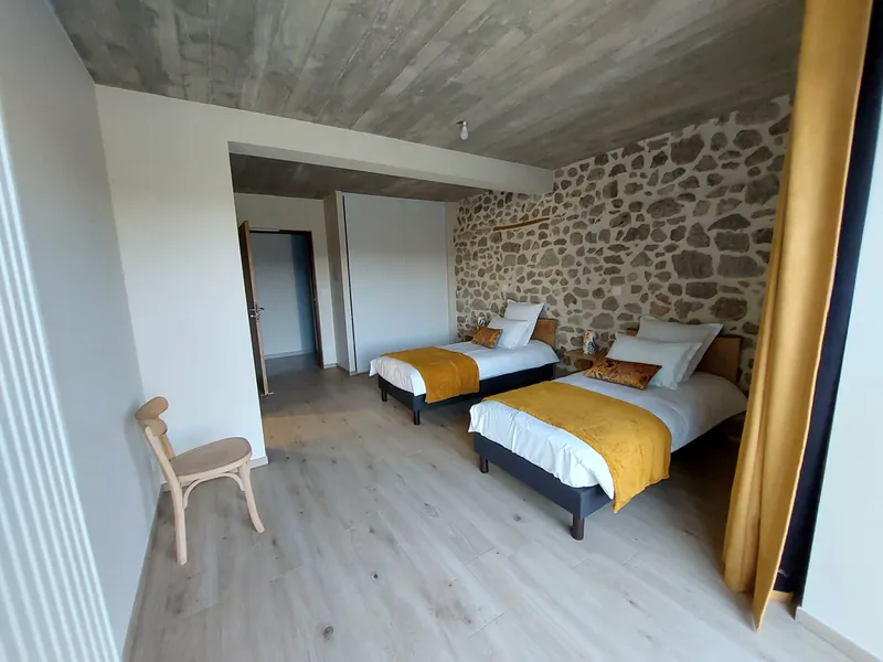 Chambre lumineuse avec deux lits simples et mur en pierres apparentes