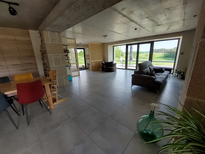 Salon avec canapés face à une baie vitrée ouverte sur la terrasse et les prairies