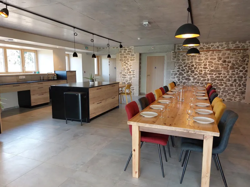 Grande table en bois dressée pour un repas de groupe face à une cuisine ouverte