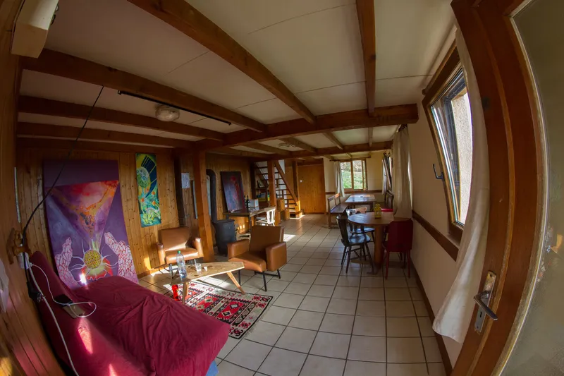 Grande salle de vie commune avec fauteuils en cuir, table ronde en bois et poêle à bois pour les soirées de groupe